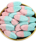 Pink and light blue candy-coated gumdrops piled in a round gold tin on a white background.