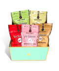 A gift box filled with six colorful Ranchor's tea bags in different flavors: Cinnamon (red), Watermelon Pillow (pink), Deer Pillow (tan), Old Fashioned (dark brown), Old Fashioned (light green), and Old Fashioned (cream). The box is mint green with gold trim on a white background.