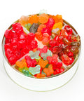 A round white tin filled with assorted colorful gummy candies, including red, orange, green, and brown gummy bears and butterflies, photographed on a clean white background.