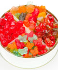 A round white tin filled with assorted colorful gummy candies, including red, orange, green, yellow, and butterfly-shaped gummies, photographed on a white background.