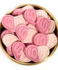 Pink and white heart-shaped candy pieces with the word 'LOVE' embossed on them, arranged inside a round gold-colored bowl on a white background.