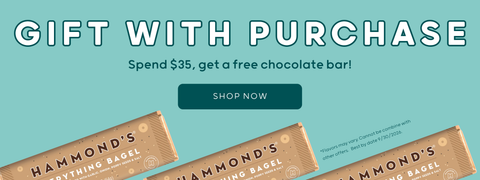 Promotional banner for Hammond's Anything Bagel featuring the text 'GIFT WITH PURCHASE' and 'Spend $35, get a free chocolate bar!' on a light blue background, with three bagel wrappers shown along the bottom and a dark green 'SHOP NOW' button.